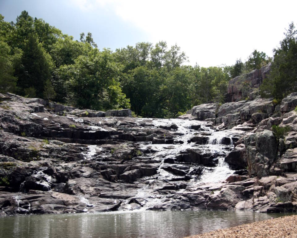 Few places in the Ozarks provide a glimpse of earth’s turbulent past as well as the Rocky Falls with its reddish-brown rock formed when molten rock deep within the earth and flowed onto the surface about 1.5 billion years ago. (Image created by USA Patriotism! from U.S. National Park Service photo by Neal Lewis.)